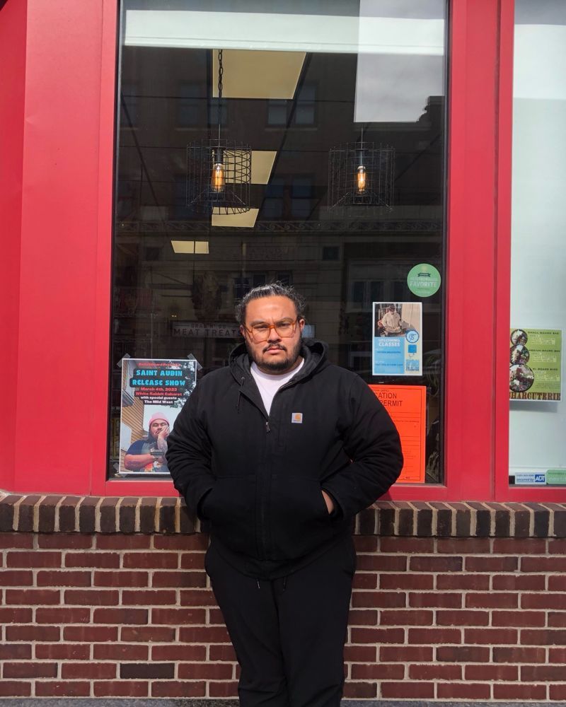 Trevor leaning on a red storefront window downtown